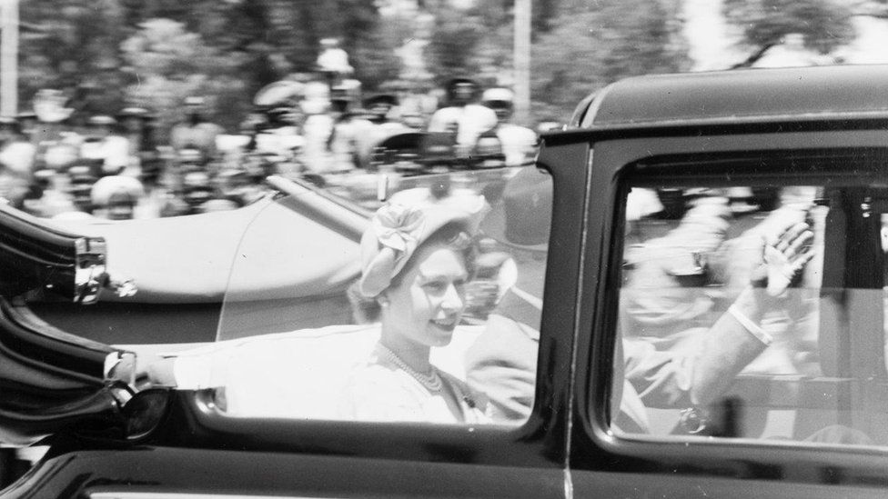 Мимо камеры проносится автомобиль с открытым верхом, в котором принцесса Елизавета и герцог Эдинбургский едут к мэрии Найроби, Кения, во время их турне по Содружеству
