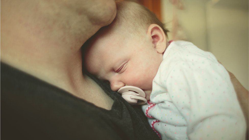 A newborn baby resting on its dad's shoulder