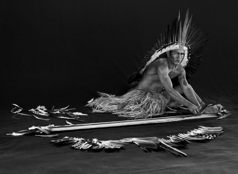 Black and white photograph of a man making feather adornments