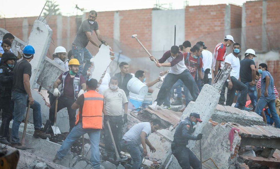 Rescuers with helmets and pickaxes clear rubble from damaged buildings