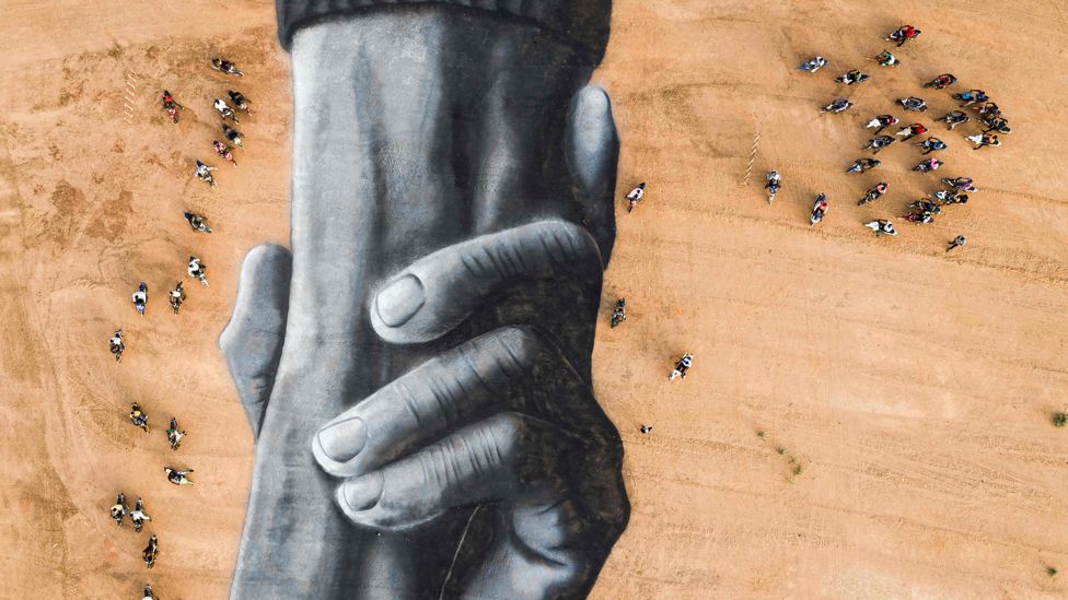 Motorcyclists surround French artist Saype's Beyond Walls artwork of interlocking hands in Ouagadougou, Burkina Faso - Sunday 1 March 2020
