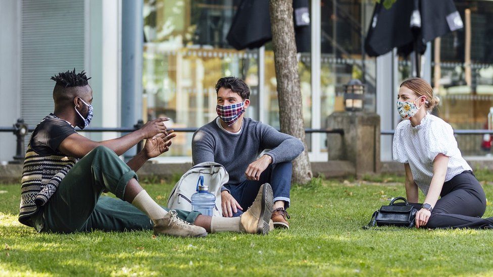 Three friends chat at a social distance while wearing face coverings