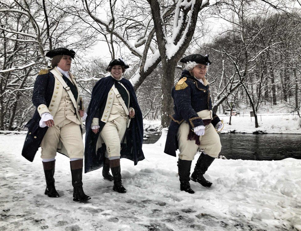 Three people wear American Revolution outfits while walking in snow