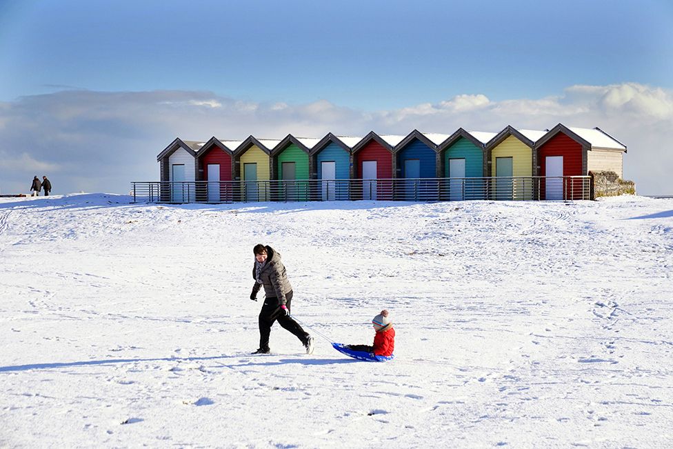 A pistillate   pulls a kid  connected  a sledge done  the snowfall  beside the formation  huts astatine  Blyth successful  Northumberland