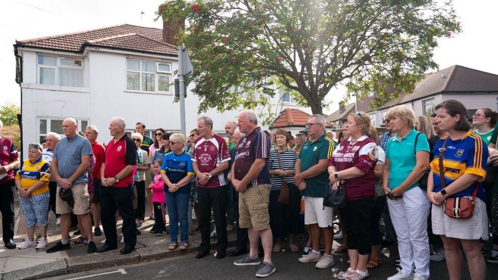 Members of the Irish community gather on Cayton Road in Greenford, Ealing, west London to pray and lay flowers in tribute to Thomas O'Halloran, 87.