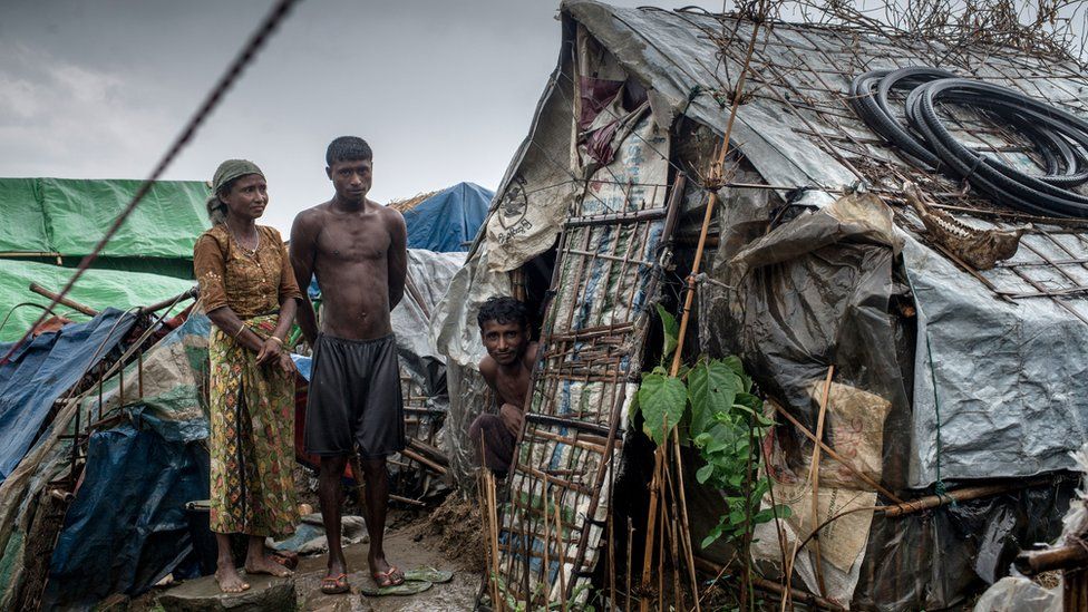 A family stands outside their hut in one of the unregistered IDP camps, May 24, 2015 in Sittwe, Myanmar. Since 2012, the minority group of the Rohingya people are forced to live in IDP camps, in Rakhine State in western Burma