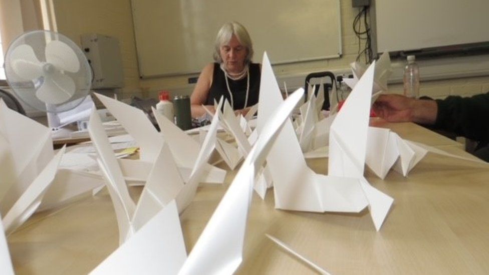 Helen sat at one end of a table, with the camera submerged in lots of white paper birds