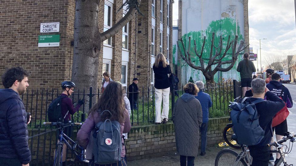 Crowd of people standing in front of suspected Banksy mural
