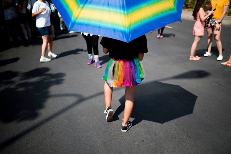 A woman marches in a rainbow-coloured skirt and parasol.