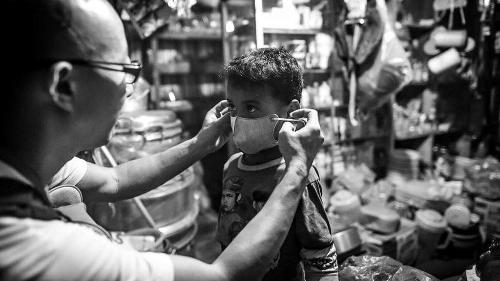 A volunteer helps a child put on an N95 face mask