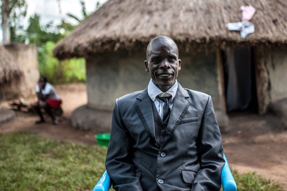 Simon Peter Otoyo sits outside his house in a blue chair
