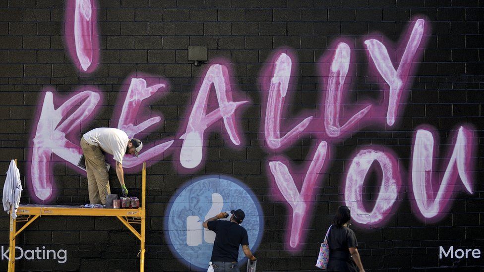 Three men spray-paint a Facebook dating advert which reads "I Really (Facebook like icon) you"