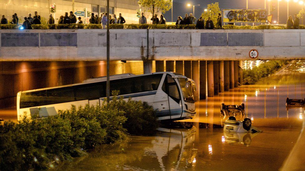 People look on a bus and cars submerged in a flooded road, in Mandra, near Athens