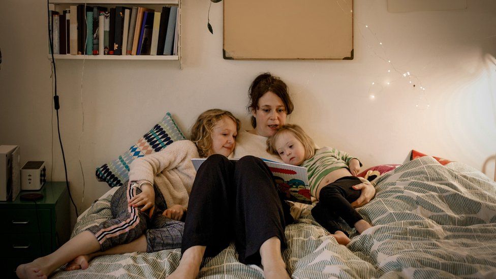 Mother reading picture book while sitting with children in bedroom - stock image