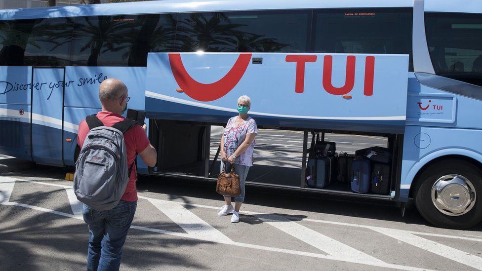 A masked Tui customer poses beside one of the firm's coaches in Spain