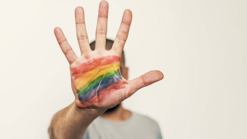 A man holding up a hand with a LGBT rainbow flow painted on his palm