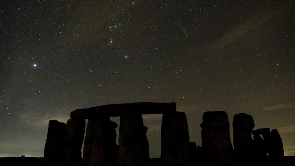 Stars sparkle in the sky above Stonehenge - the trail of one meteor streaks about