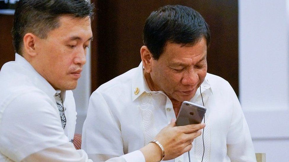Filipino President Rodrigo Duterte (R), assisted by Special Assistant to the President Christopher Lawrence Go (L), speaking to US President Donald J. Trump during a phone call on the sidelines of the gala dinner