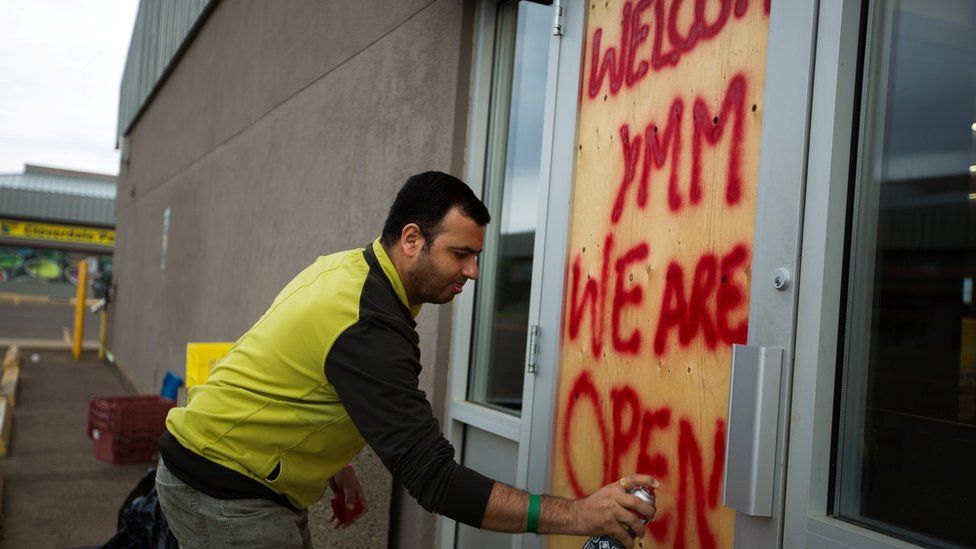 Convenience store manager Sunny Katoch paints a welcome sign on the back door as residents begin to flood back into their city after being evacuated due to raging wildfires in Fort McMurray, Alberta, Canada, 1 June 2016.