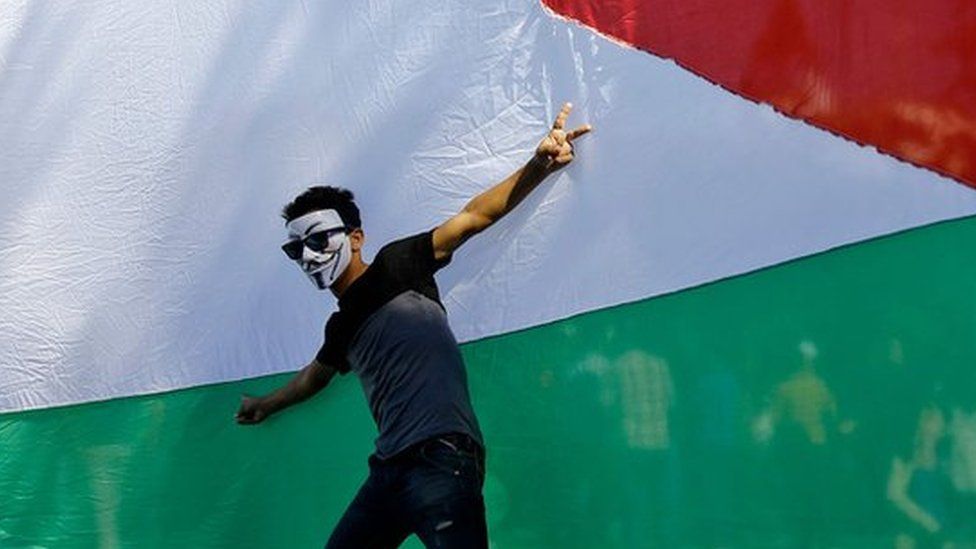 A Palestinian youth poses in front of his national flag during celebrations in Gaza City after rival Palestinian factions Hamas and Fatah reached an agreement on ending a decade-long split, 12 October 2017