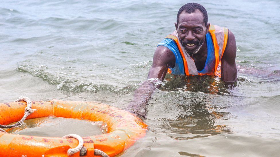 Lifeguard Nicholas Paul swimming with a lifebuoy in Lagos, Nigeria