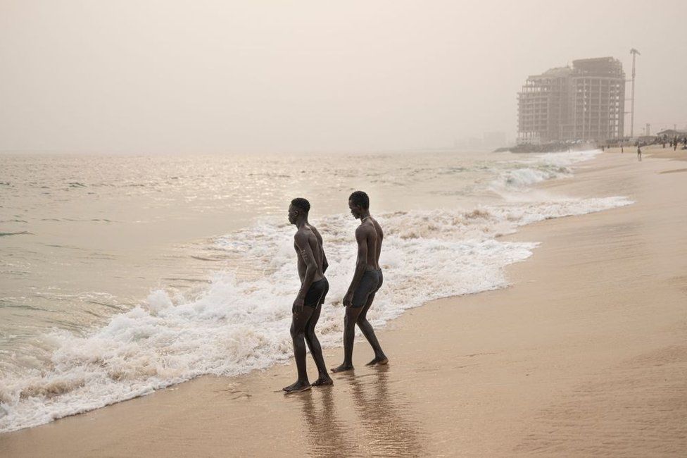 Two men walk towards the sea at a beach in Lagos.