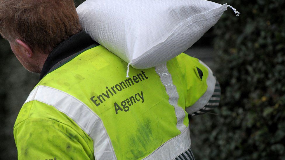 An Environment Agency worker carries a sandbag at the river Parrett in Burrowbridge, Somerset, as flooding persists on the levels.