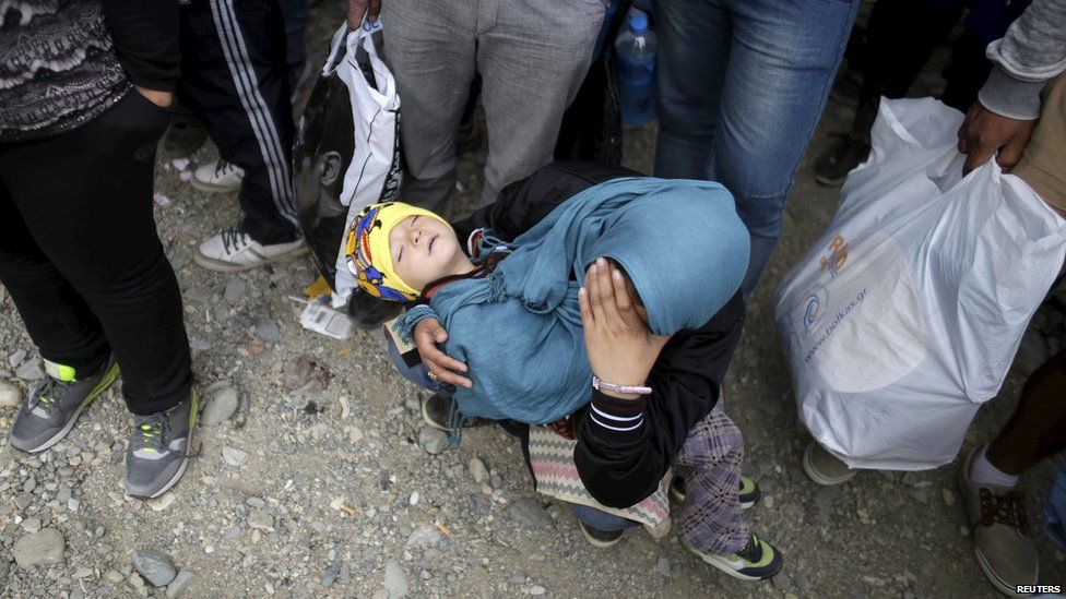 A migrant holds a child as they wait to board a train after crossing the Macedonian-Greek border near Gevgelija, Macedonia, on 8 September 2015