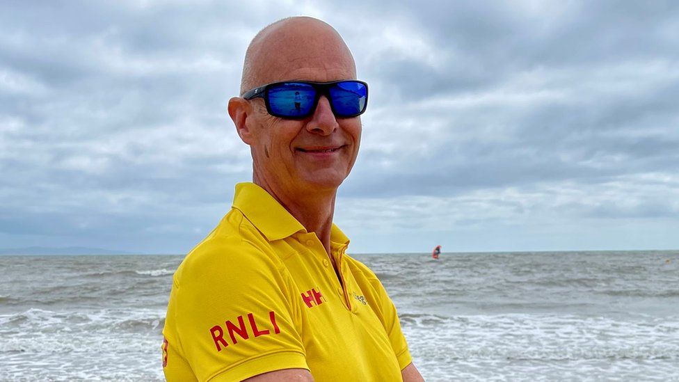 Lifeguard Malcolm Greenslade wearing a yellow RNLI t-shirt with the sea in the background