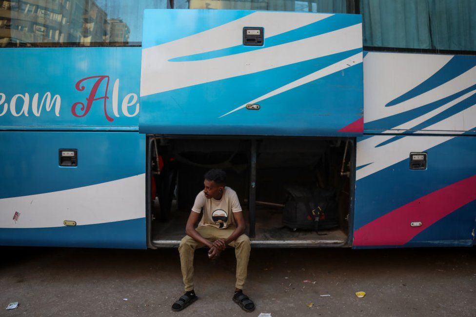 A Sudanese man waits at a bus stop in downtown Cairo to return to his family with food.