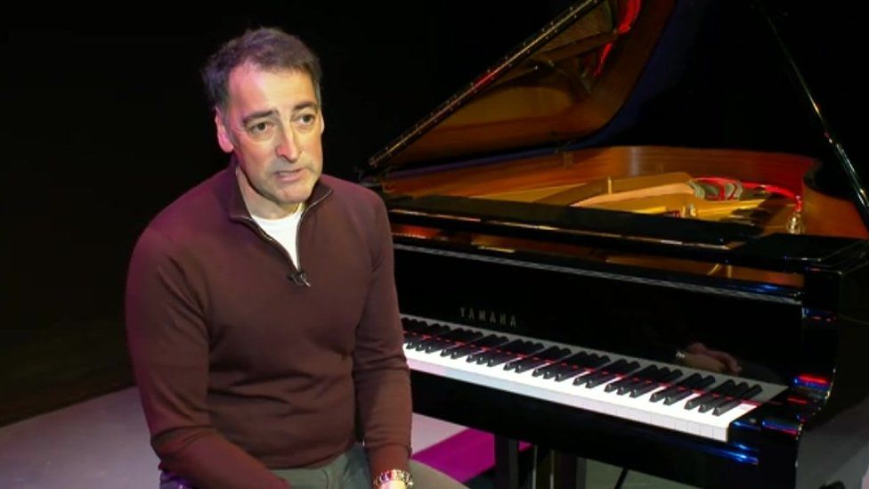 Alistair McGowan sitting in front of a piano