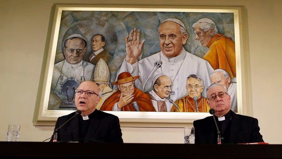 Chilean bishops Luis Fernando Ramos Perez and Juan Ignacio Gonzalez Errazuriz holding a news conference in front of a painting of the Pope