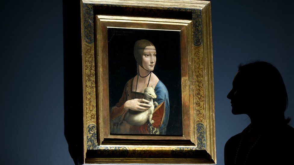 a woman posing for pictures beside a painting entitled "Portrait of Cecilia Gallerani" (The Lady with an Ermine) by Italian artist Leonardo da Vinci, London