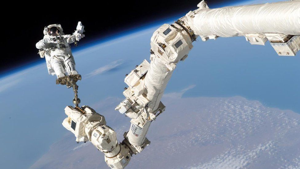 An astronaut suspended by an arm above the surface of planet Earth.