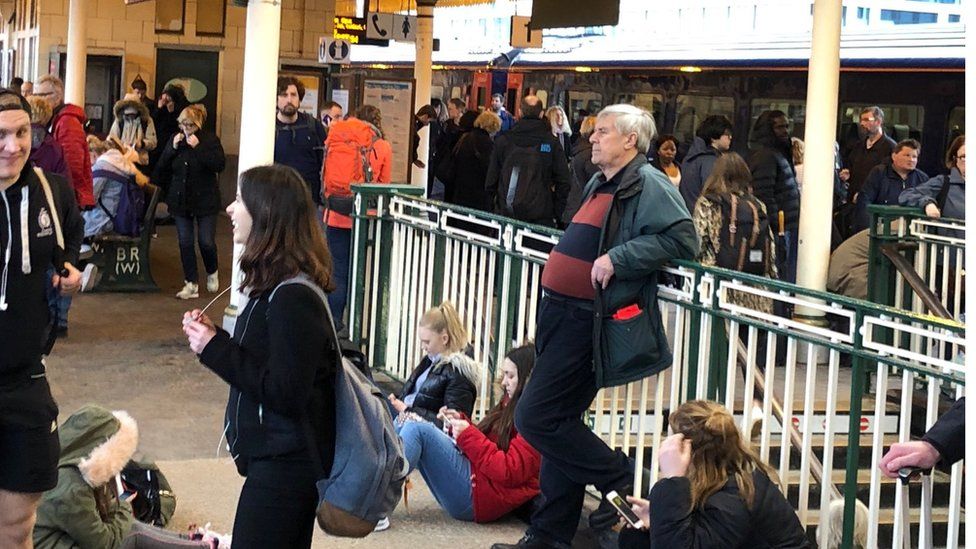 Passengers sit on the ground at Cardiff Central station as trains are delayed or cancelled