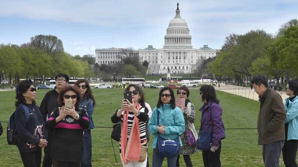 A group of Chinese tourists take photographs on the National Mall with the U.S. Capitol in the background