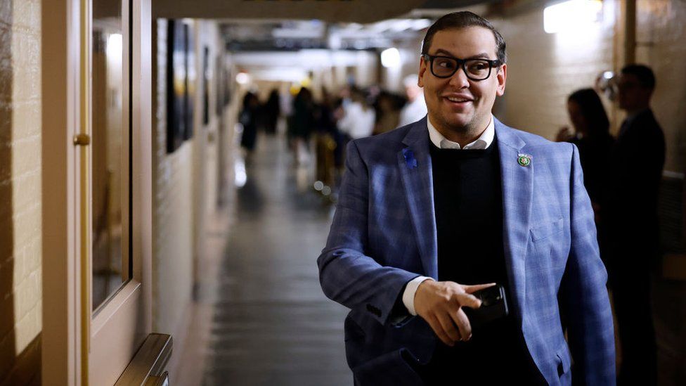George Santos in blue checked jacket walks in Capitol Hill hallway.