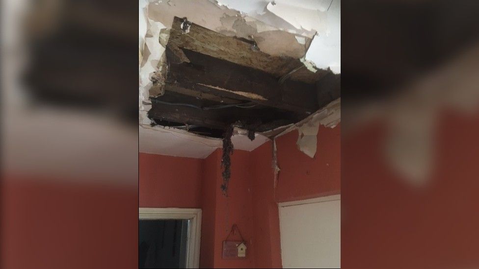Hole in ceiling revealing floor boards and electric cables