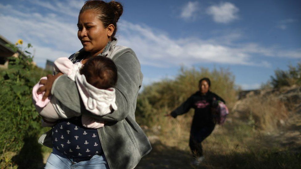 An immigrant mother crosses the US southern border with a baby in her arms.