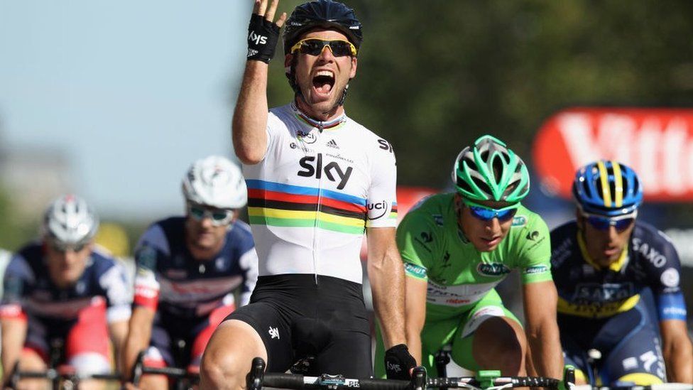 Mark Cavendish, wearing a Team Sky jersey, holds up his right hand as he crosses the line at the 2012 Tour de France