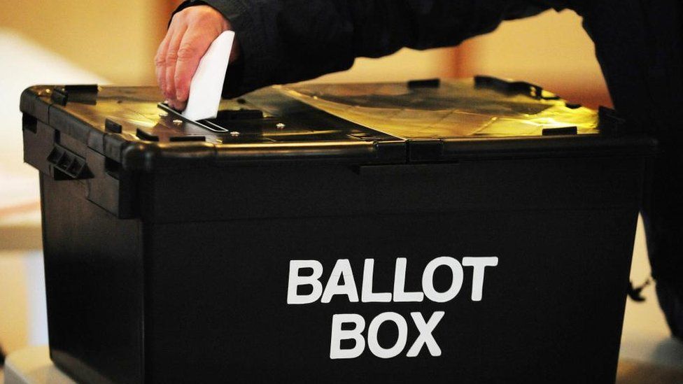 A stock image of a voter putting a piece of paper into a ballot box