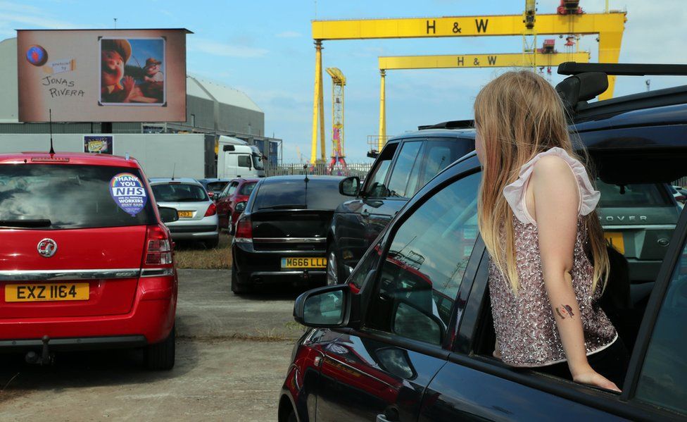 A girl leans out of a car to watch the screen at a drive-in cinema