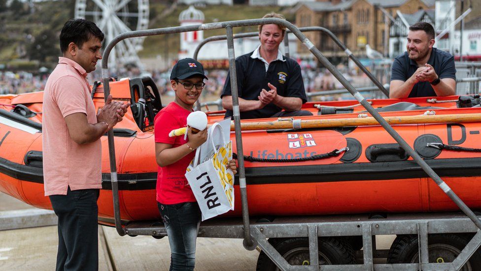Ravi Saini looking at a toy he has taken out of a bag in front of RNLI crew and his dad