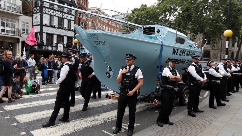 Police stand in front of a boat used by climate change protesters to block a road in London