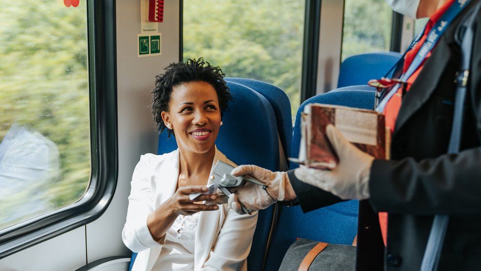 A lady smiling on a train handing her ticket to the inspector