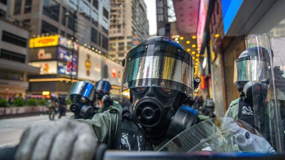 A riot police officer pushes journalist away using his baton.