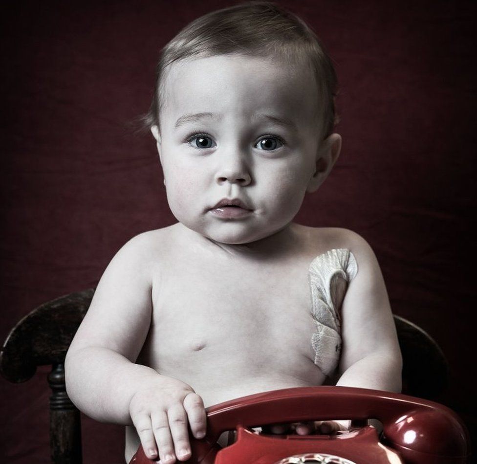 A very young boy holds a phone