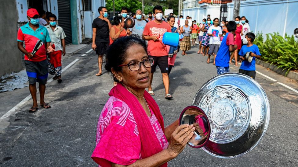 A woman in a protest against food price hikes bangs dishes together.
