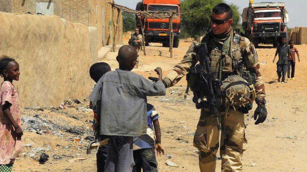 A soldier of France's Barkhane mission stands next to children as he patrols in In-Tillit on November 1, 2017 in Mali
