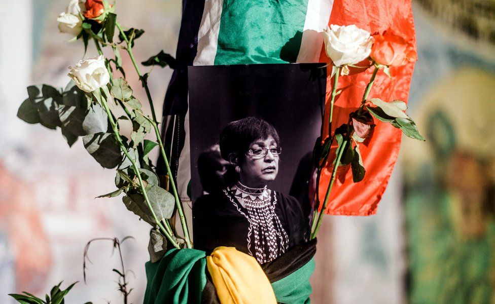 A black and white photograph of the late Winnie Madikizela-Mandela is surrounded by the South African and African National Congress (ANC) flags on a pole at the Old Durban Prison's Human Rights wall as South Africans gather to pay respect to the late high-profile anti-apartheid activist during a candle vigil in Durban on April 2, 2018.
